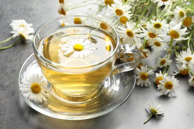 Lezzetli papatya çayı ve çiçekler gri masada, yakın plan.