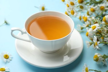 Lezzetli papatya çayı ve açık mavi arka planda çiçekler, yakın plan.