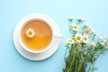 Lezzetli papatya çayı ve çiçekler açık mavi arka planda, düz yerde
