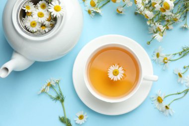 Lezzetli papatya çayı ve çiçekler açık mavi arka planda, düz yerde