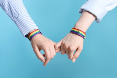 LGBT konsepti. Gökkuşağı bileklikli kadınlar açık mavi arka planda el ele tutuşuyorlar, yakın plan.