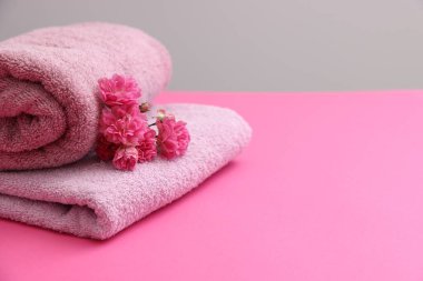 Pembe masadaki yumuşak havlular ve çiçekler gri arka plana karşı, yakın plan. Metin için boşluk