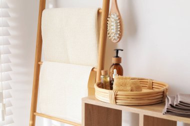 Banyodaki beyaz duvarın yanındaki raflarda temiz waffle havluları ve spa ürünleri var.