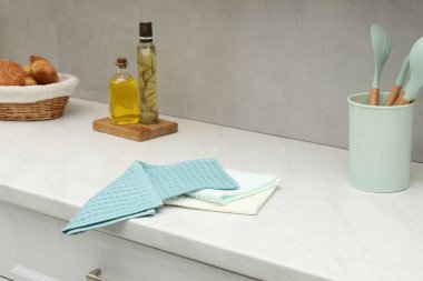 Gri duvarın yanındaki beyaz tezgahta waffle havluları ve mutfak malzemeleri var.