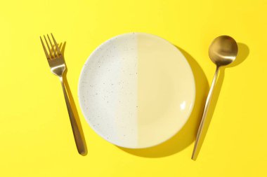 Sarı arka planda şık bir tabak ve çatal bıçak takımı.