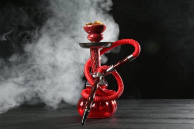 Siyah arka planda duman olan ahşap masada nargile.
