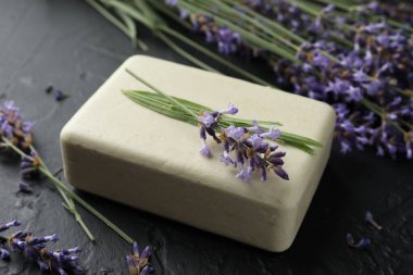 Aromatik sabun barı ve lavanta çiçekleri koyu dokulu masa üzerinde, yakın plan.