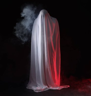 Ürkütücü hayalet. Siyah arka planda beyaz bir çarşafla kaplanmış bir adam.