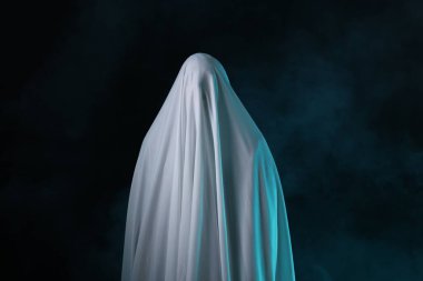 Ürkütücü hayalet. Siyah arka planda beyaz bir çarşafla kaplanmış bir adam.