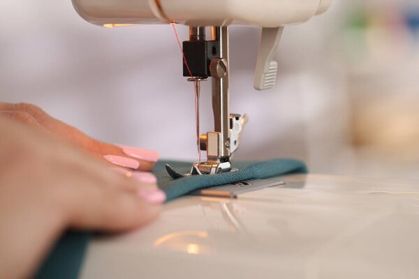 Женщина работает с швейной машинкой и тканями в мастерской, крупным планом