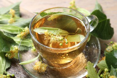 Fincanda lezzetli ıhlamur çayı, masada yapraklar ve çiçekler, yakın plan.