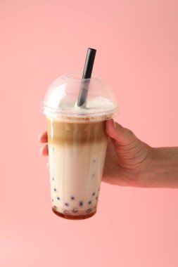 Pembe arka planda lezzetli sütlü çay içen kadın, yakın plan.