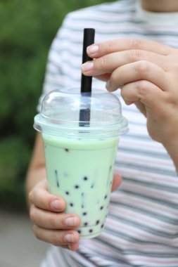 Dışarıda plastik bardakta lezzetli sütlü çay içen kadın, yakın plan.