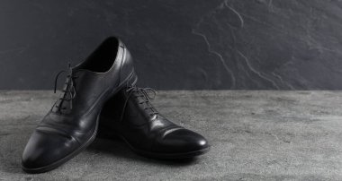 Gri yüzeyde bir çift siyah deri ayakkabı, yakın plan. Metin için boşluk