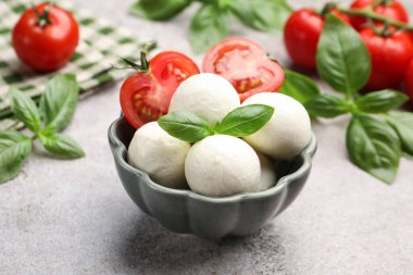 Lezzetli mozzarella peynir topları, domates ve fesleğen gri masada, yakın plan.