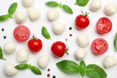 Lezzetli mozzarella peyniri topları, domatesler, fesleğen ve biberler beyaz arka planda, düz yayılmış