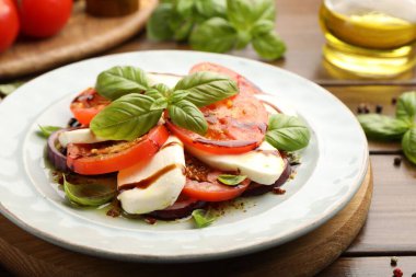 Mozarella, domates, fesleğen ve baharatlarla ahşap masaya yakın plan Caprese salatası.