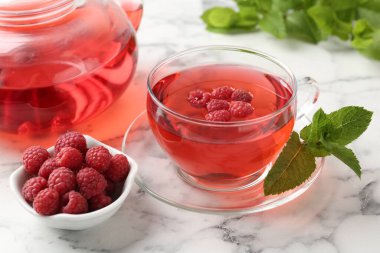 Lezzetli ahududu çayı, böğürtlen ve yapraklar beyaz mermer masada, yakın plan.