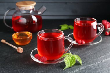 Cam bardaklarda Aromatik ahududu çayı, çaydanlık, böğürtlen, yeşil yapraklar ve bal siyah masada, yakın plan