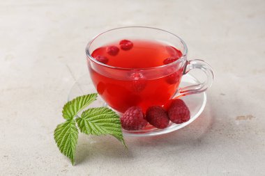 Cam bardakta lezzetli ahududu çayı, açık gri masada yeşil yapraklar, yakın plan.