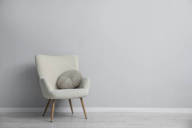 Açık gri duvarın yanında rahat bir koltuk ve yastık. Metin için boşluk