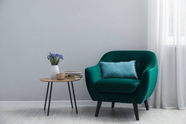 Açık gri duvarın yanında rahat bir koltuk ve dekor.