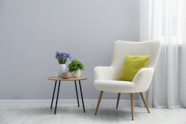 Açık gri duvarın yanında rahat bir koltuk ve dekor.