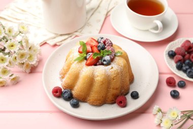 Pudra şekerli, böğürtlenli ve nane şekerli nefis kek, pembe ahşap masa, yakın plan.