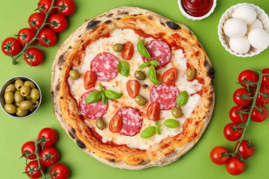 Lezzetli pizza ve malzemeler yeşil masada, düz yerde.