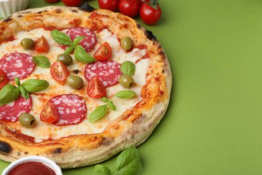 Yeşil masada salamlı, zeytinli, domatesli ve fesleğenli lezzetli pizza. Metin için boşluk