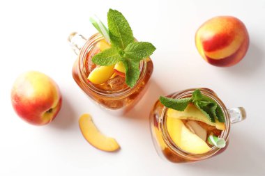 Buzlu şeftali çayını mason kavanozlarında nane ve beyaz masada taze meyveler ile tazeliyorum.