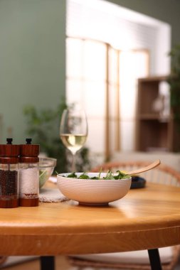 Bir kase salata, beyaz şarap ve baharatlar masanın içinde.