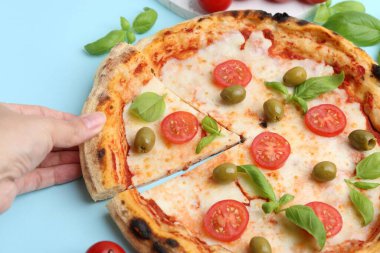 Açık mavi masada lezzetli bir pizza yiyen kadın, yakın plan.