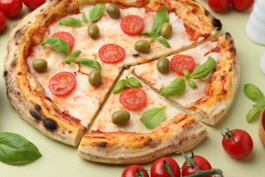 Açık yeşil arka planda domatesli, fesleğenli ve zeytinli pizza, yakın plan.