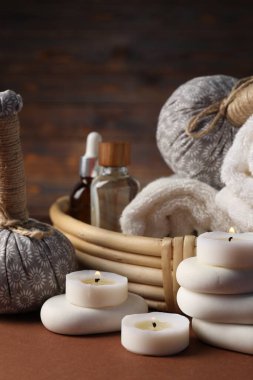 Masaj çantaları, taşlar, havlular, kozmetik ürünler ve koyu bej masa üzerinde yanan mumlar, yakın plan. Spa bileşimi