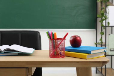 Farklı okul kırtasiyesi ve kırmızı elma, kapalı alanda tahtaya yakın ahşap masada.