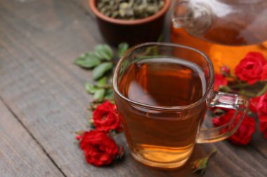 Cam fincanda lezzetli bir gül çayı, tahta masada çiçekler ve yapraklar, yakın plan.