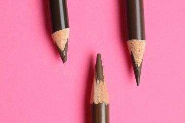 Pembe arka planda farklı kaş kalemleri, düz yatış.