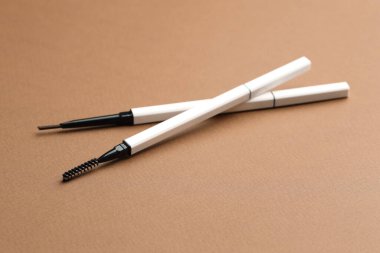 Kahverengi arka planda otomatik kaş kalemleri, yakın plan.