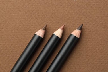 Kahverengi arka planda farklı kaş kalemleri, düz yatış.