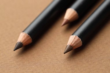 Kahverengi arka planda farklı kaş kalemleri, yakın plan.