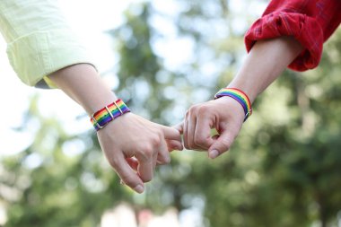 LGBT konsepti. Gökkuşağı bileklikli kadınlar dışarıda el ele tutuşuyorlar, yakın plan.