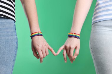 LGBT konsepti. Gökkuşağı bileklikli kadınlar yeşil arka planda el ele tutuşuyorlar, yakın plan.