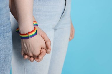 LGBT konsepti. Gökkuşağı bileklikli kadınlar açık mavi arka planda el ele tutuşuyorlar, yakın plan. Metin için boşluk