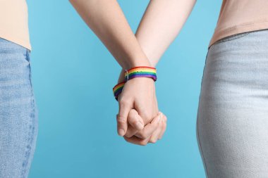 LGBT konsepti. Gökkuşağı bileklikli kadınlar açık mavi arka planda el ele tutuşuyorlar, yakın plan.