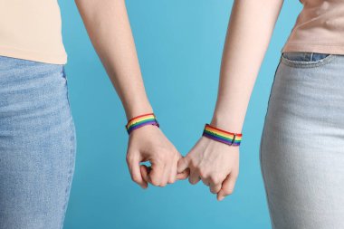 LGBT konsepti. Gökkuşağı bileklikli kadınlar açık mavi arka planda el ele tutuşuyorlar, yakın plan.