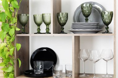 Beyaz duvarın yanında farklı bulaşık takımları, gözlük ve çiçek dekoru olan raf ünitesi.