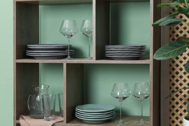 İçerideki yeşil duvarın yanında farklı bulaşık takımları ve gözlüklerle raf ünitesi.
