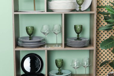 Kapalı alandaki yeşil duvarın yanında farklı plaka ve gözlüklerle raf ünitesi.