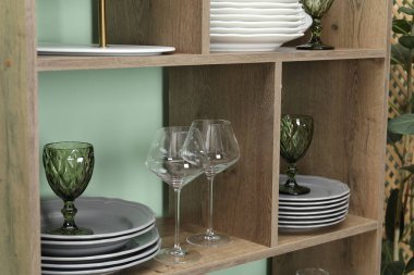 Kapalı alanda yeşil duvarın yanında farklı plakalı ve gözlüklü raf ünitesi.